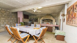 A stone-walled outdoor dining area with a round table, wooden chairs, a ceiling fan, and a pizza oven. - Apartments Pavlina (Starigrad - Paklenica)