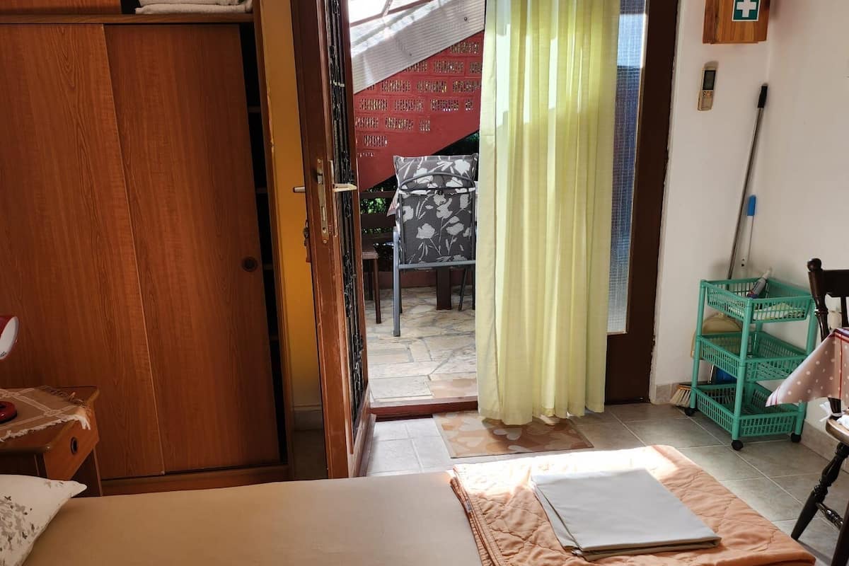 A bedroom with a bed, a wooden wardrobe, a green chair, a small table, and a curtain.
