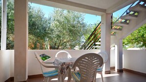A balcony with a table and chairs, a view of trees, and a staircase. - Apartments Tome (Povljana)