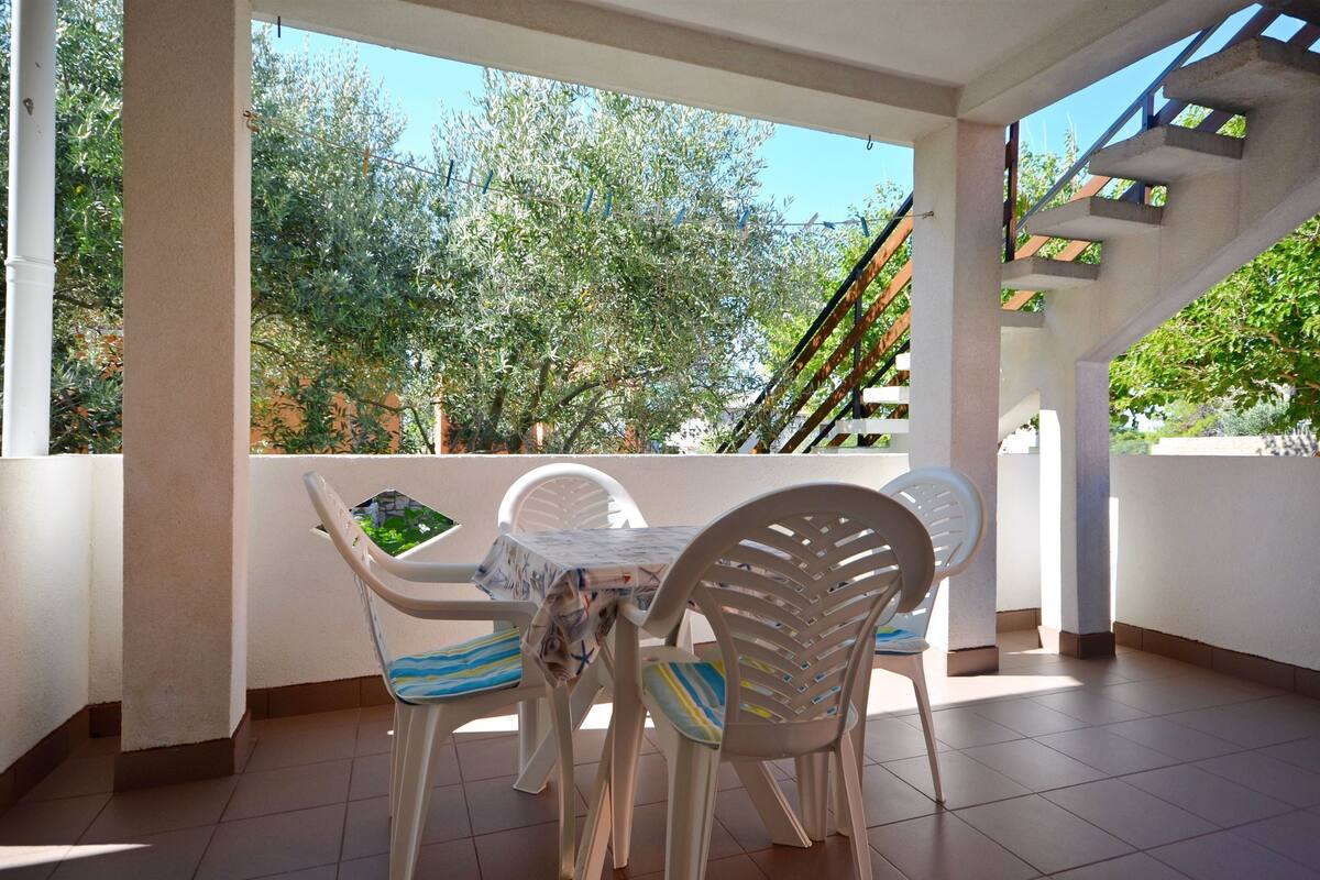 A balcony with a table and chairs, a view of trees, and a staircase.