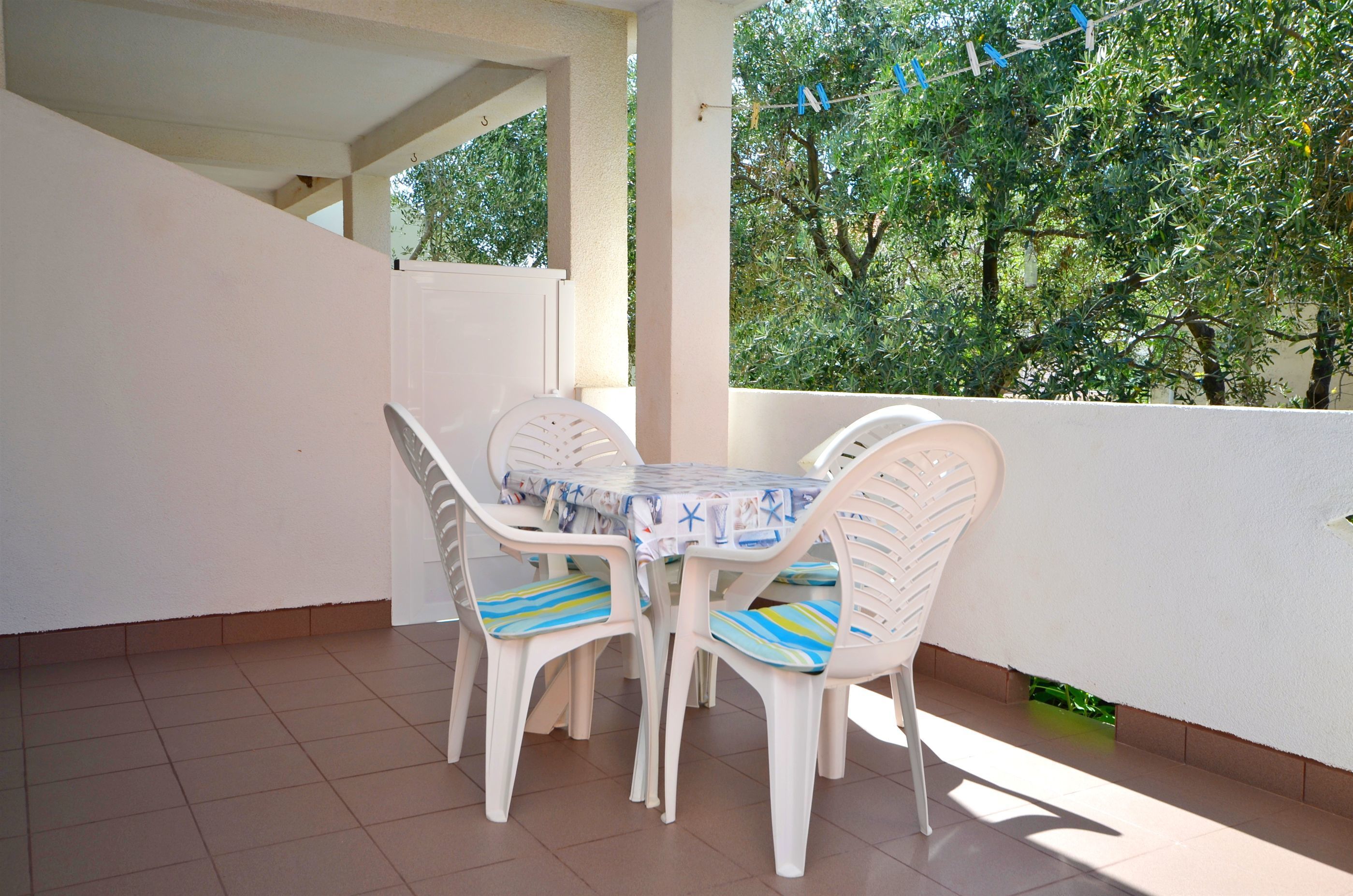 Un balcon avec une table et des chaises blanches, une vue sur les arbres et un mur blanc.