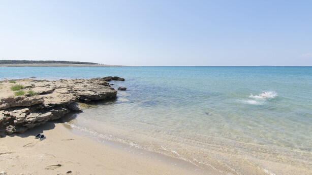 A beach with clear water, rocky shoreline, and a pair of shoes on the sand. - Apartments Tome (Povljana)