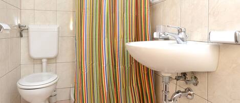 Et badeværelse med toilet, håndvask og bruseforhæng.