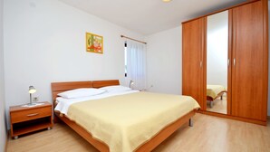 A bedroom with a wooden bed, a nightstand, a wardrobe, and a painting on the wall. - Apartments Tome (Povljana)