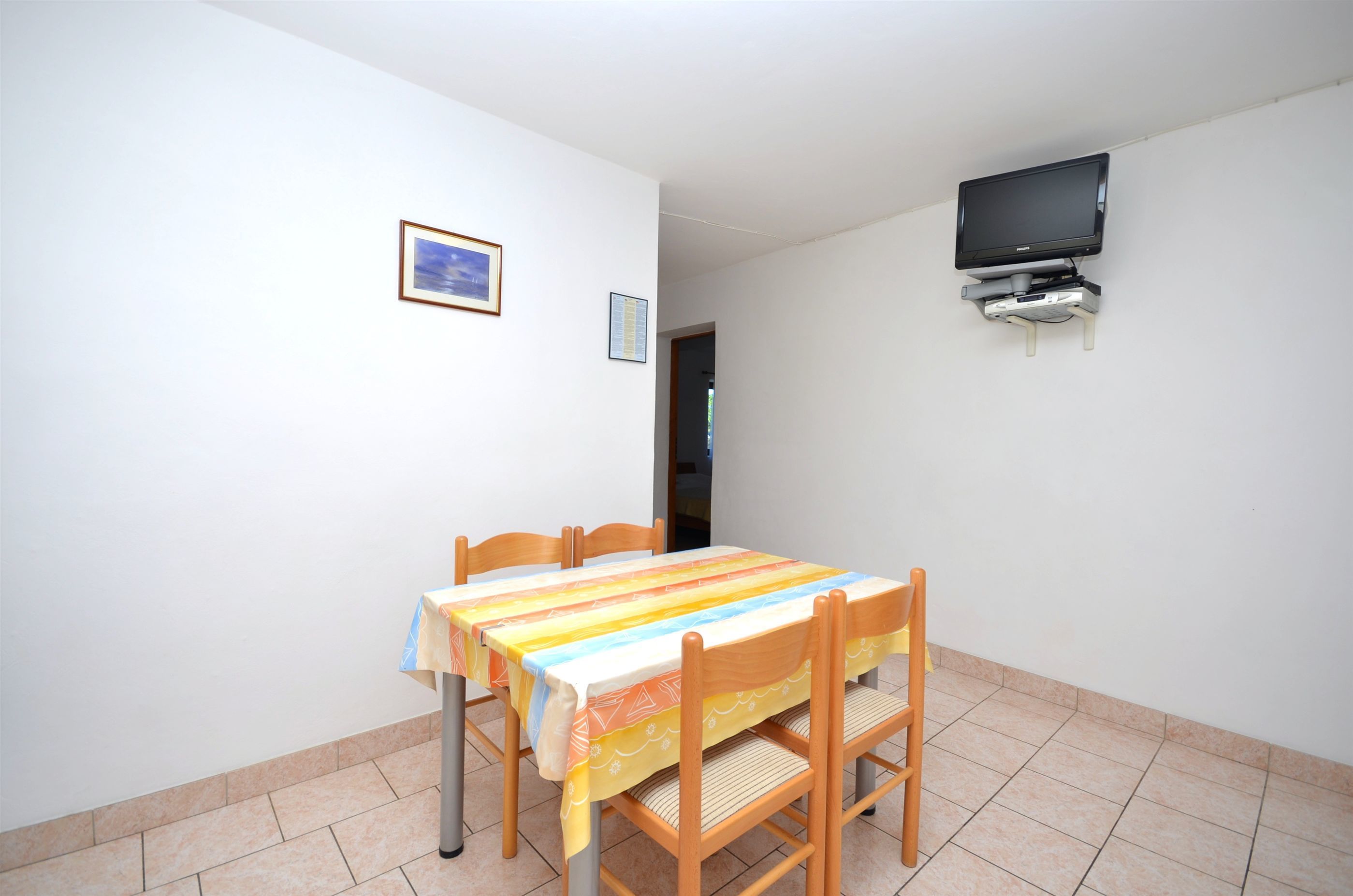 Un coin repas avec une table et des chaises, un téléviseur fixé au mur et un tableau encadré accroché au mur.