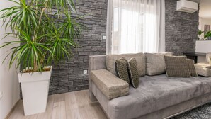 A modern living room with a grey sofa, a large potted plant, and a stone wall. - Apartments Mladen (Duce)
