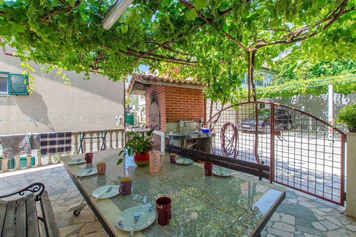 An outdoor dining area with a table set for four, surrounded by a brick wall and a metal gate.