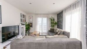 A modern living room with a grey sofa, a flat-screen TV, a coffee table, and a stone accent wall. - Apartments Mladen (Duce)