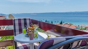 A balcony with a table set for two, overlooking a coastal view with boats and buildings. - Apartments Mladen (Duce)
