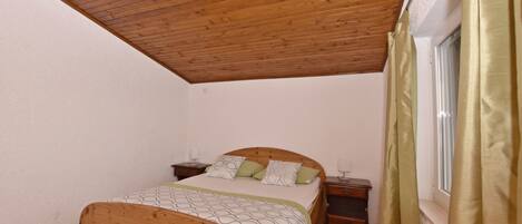 A bedroom with a wooden ceiling, a bed with a patterned bedspread, two bedside tables, and a window with curtains.