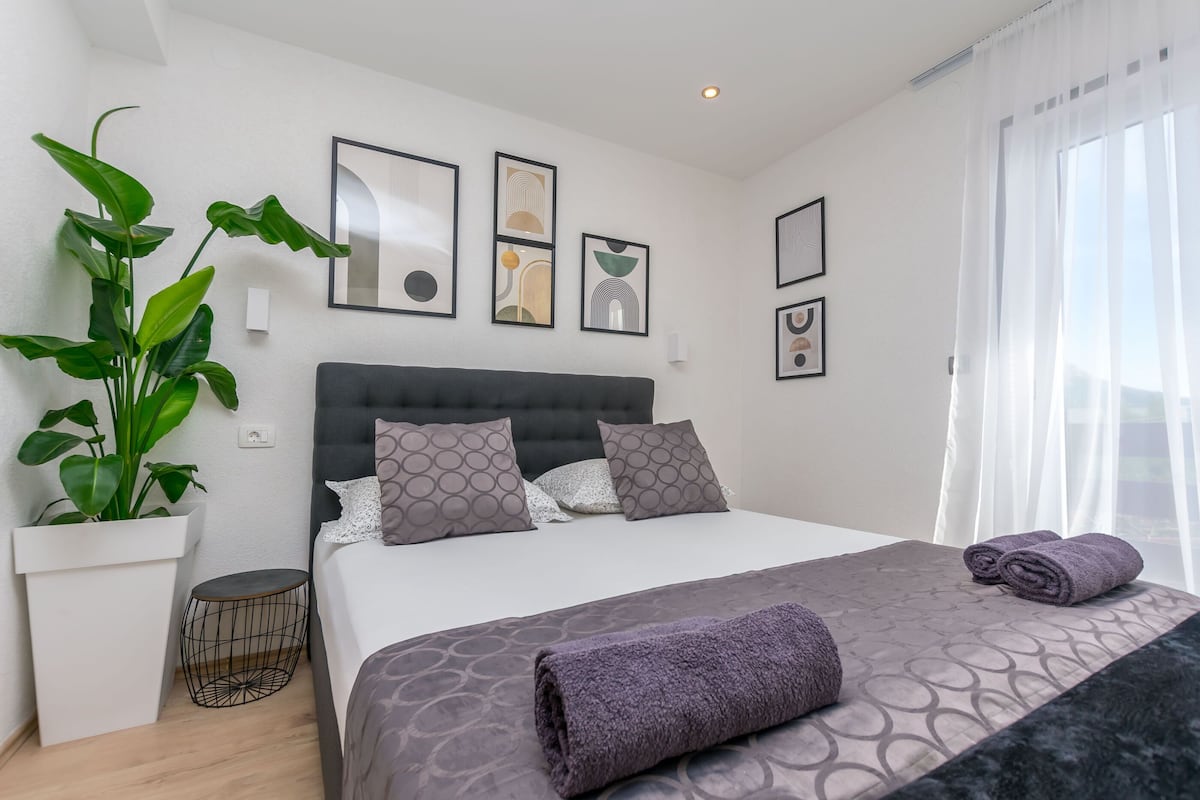 A modern bedroom with a large bed, a potted plant, and framed artwork on the wall.