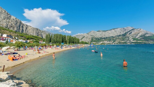 A beach with clear water, people swimming, and mountains in the background. - Apartments Mladen (Duce)