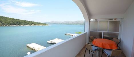 A balcony with a table and chairs, overlooking a calm lake with boats and a hilly landscape.