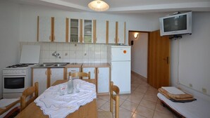 A compact kitchen with a dining table, chairs, a TV mounted on the wall, and a small oven. - Apartments Zlatko (Jadrtovac)