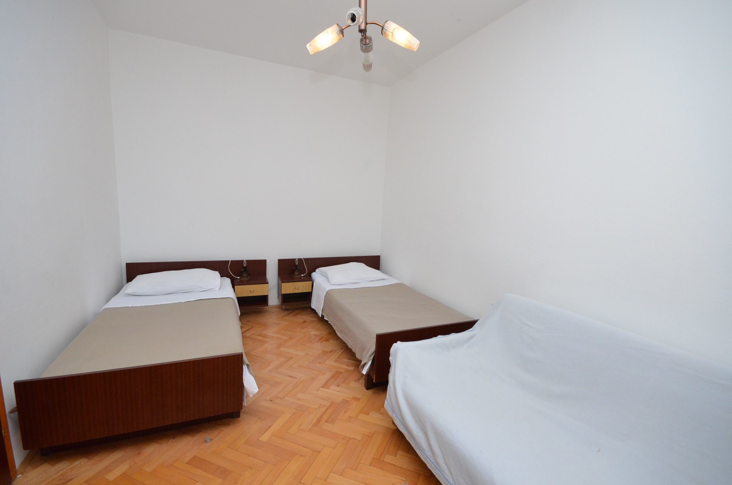 A room with two single beds, a wooden floor, white walls, and a ceiling fan.