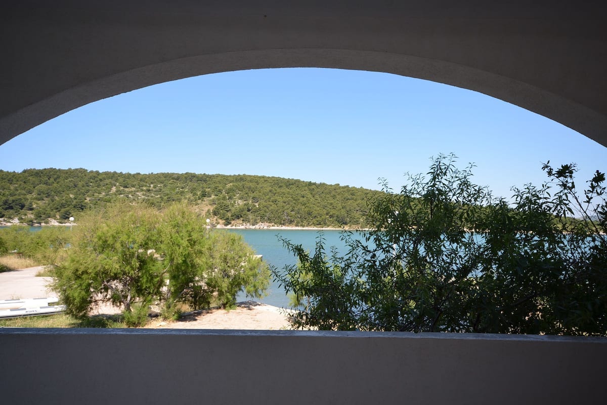Vista attraverso un arco su un lago, circondato da vegetazione e colline.