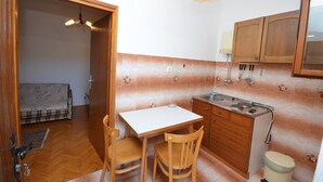 A compact kitchen with a dining table and chairs, a small sink, and wooden cabinets. - Apartments Zlatko (Jadrtovac)