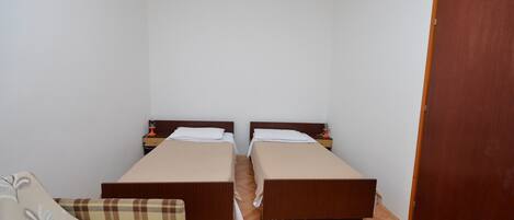Ein Zimmer mit zwei Einzelbetten, Holzboden, Holztür und einem kleinen Tisch mit Lampe.