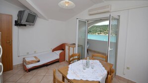 A small room with a bed, a table with a tablecloth, a TV mounted on the wall, and a balcony with a view. - Apartments Zlatko (Jadrtovac)