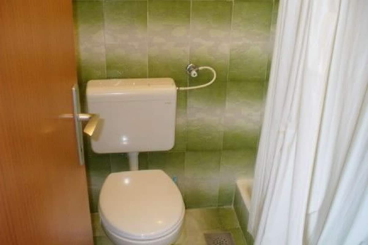 Un bagno piccolo con il water, una tenda da doccia e piastrelle verdi.