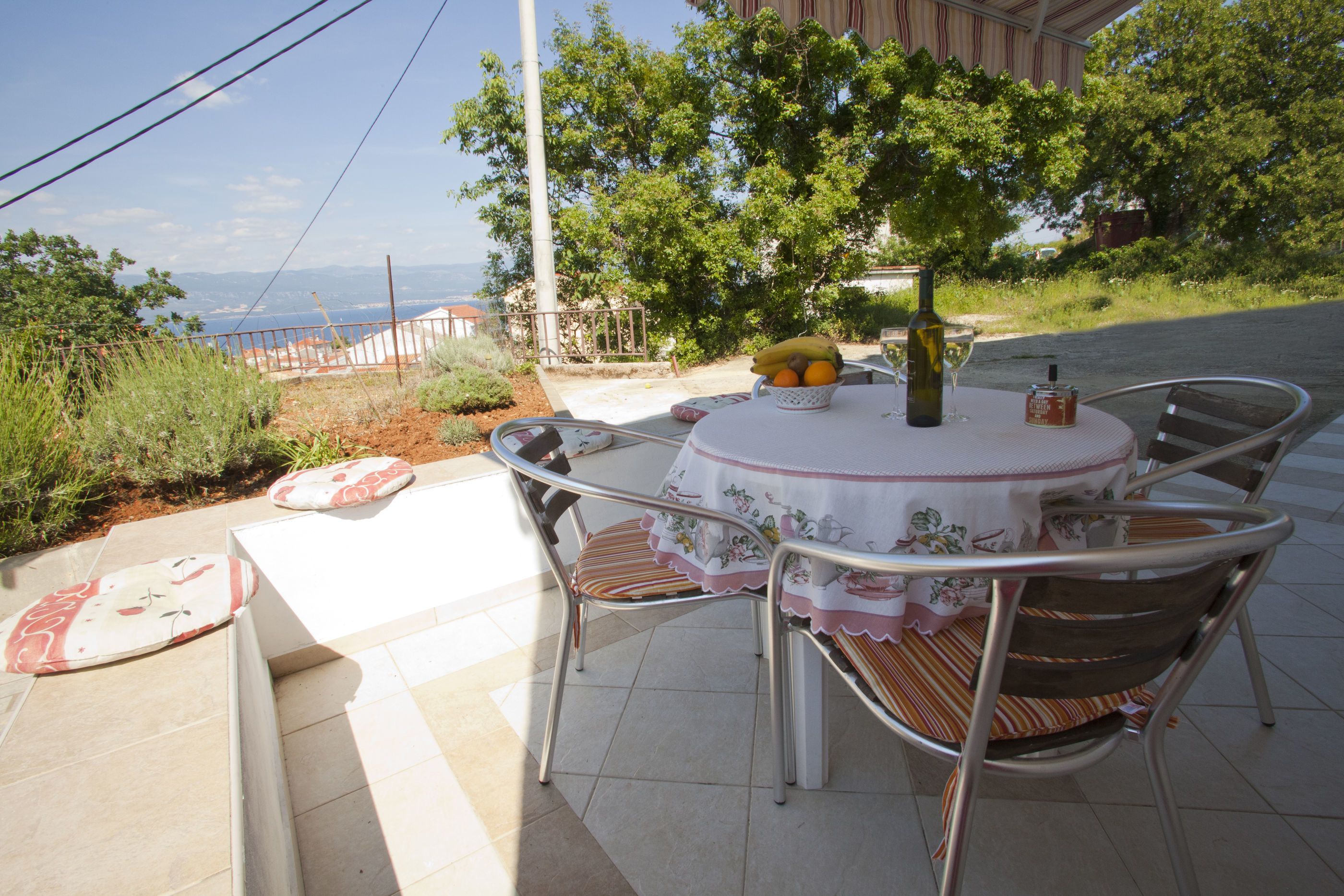 An outdoor dining area with a table and chairs, a bowl of fruit, and a bottle of wine.