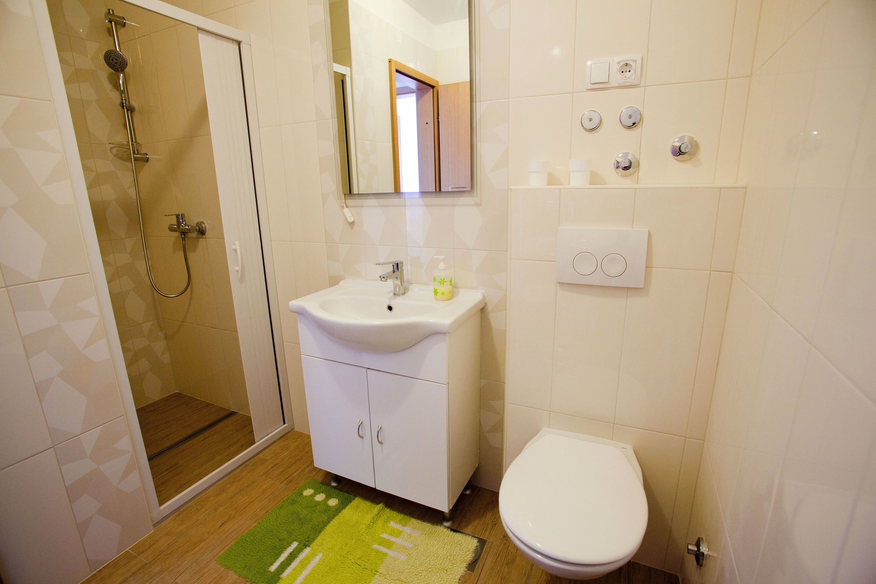 A bathroom with a shower, sink, toilet, and a mirror.