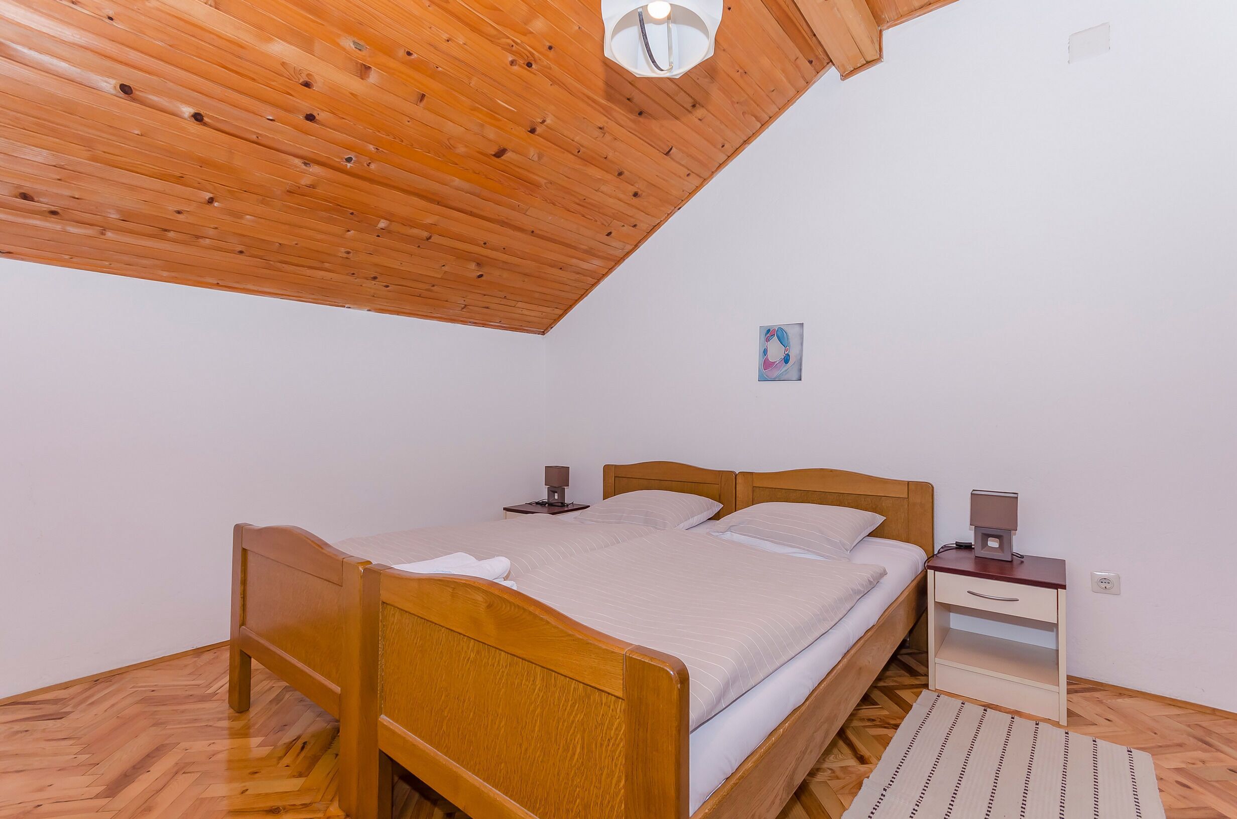 A bedroom with a wooden ceiling, a bed with a nightstand, and a small wall art piece.