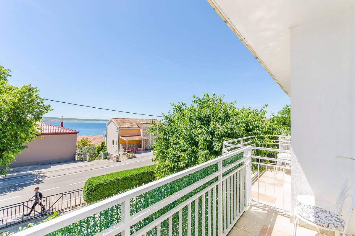 A balcony with a white railing overlooking a street, a clear blue sky, and a body of water in the distance.