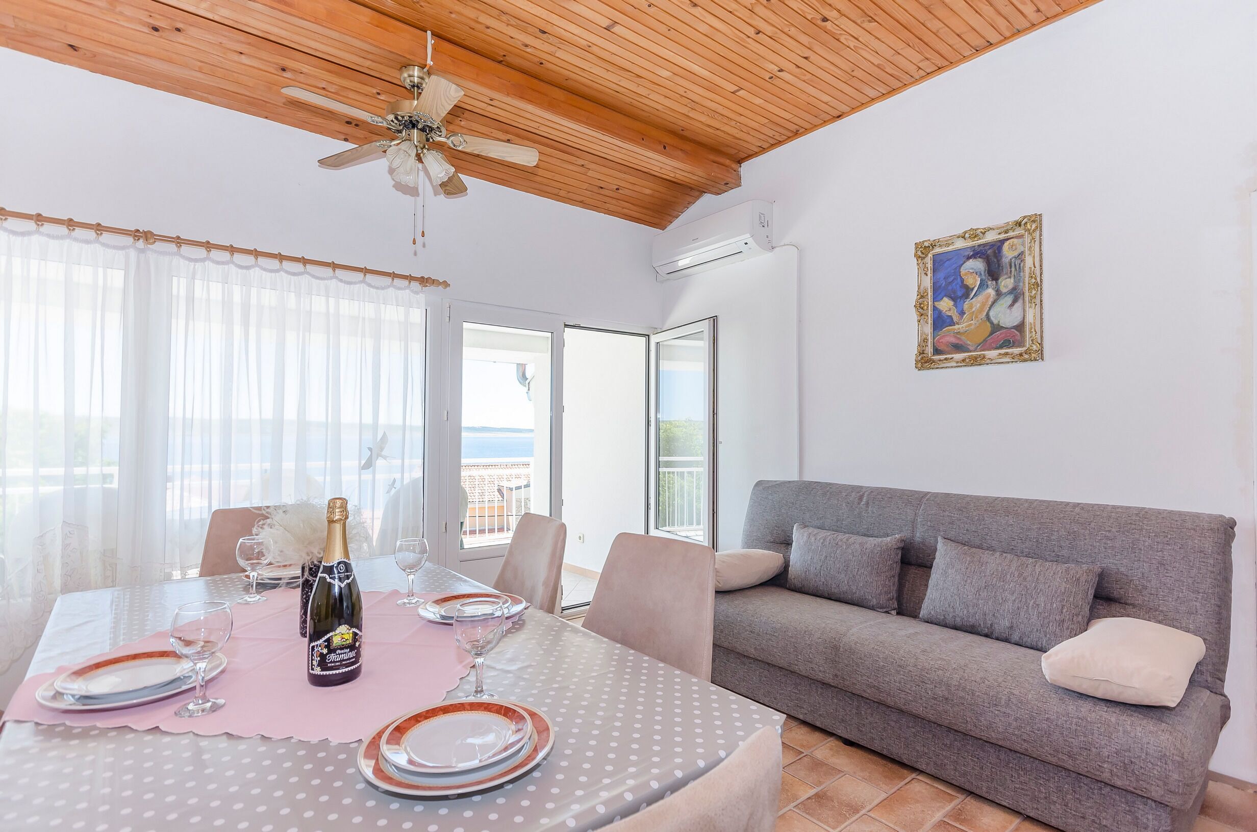 A dining area with a table set for two, a grey sofa, and a ceiling fan.