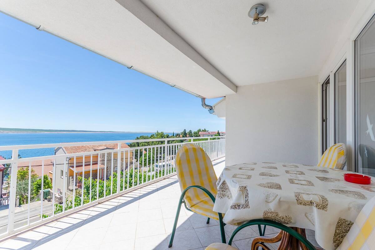 A balcony with a table and chairs, overlooking a coastal view.