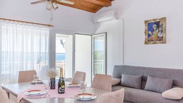 Ein Essbereich mit einem für zwei Personen gedecktem Tisch, einem grauen Sofa und Meerblick durch große Fenster.