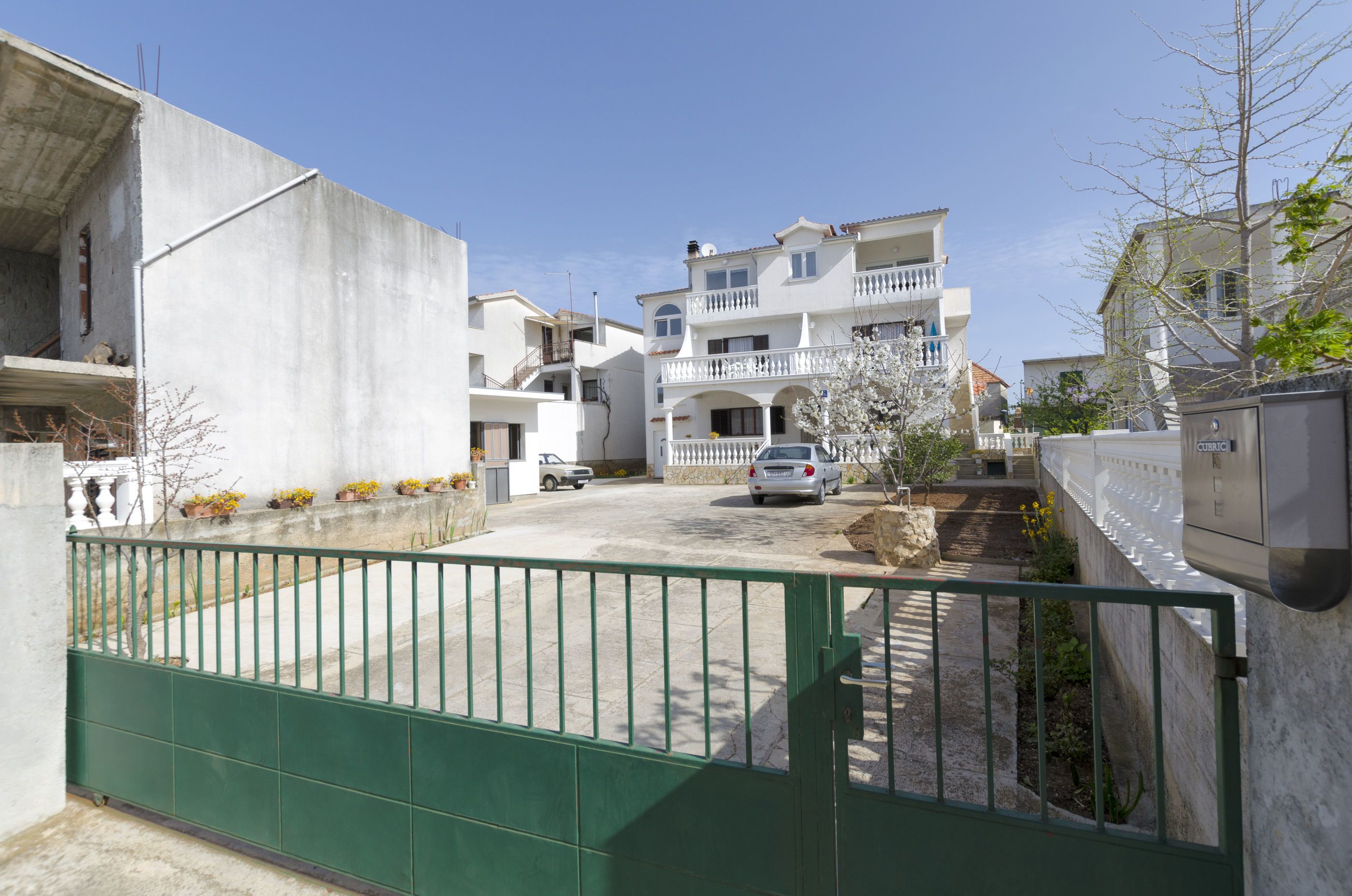 Un quartier résidentiel doté d’une entrée sécurisée, un immeuble blanc avec des balcons et une voiture garée.