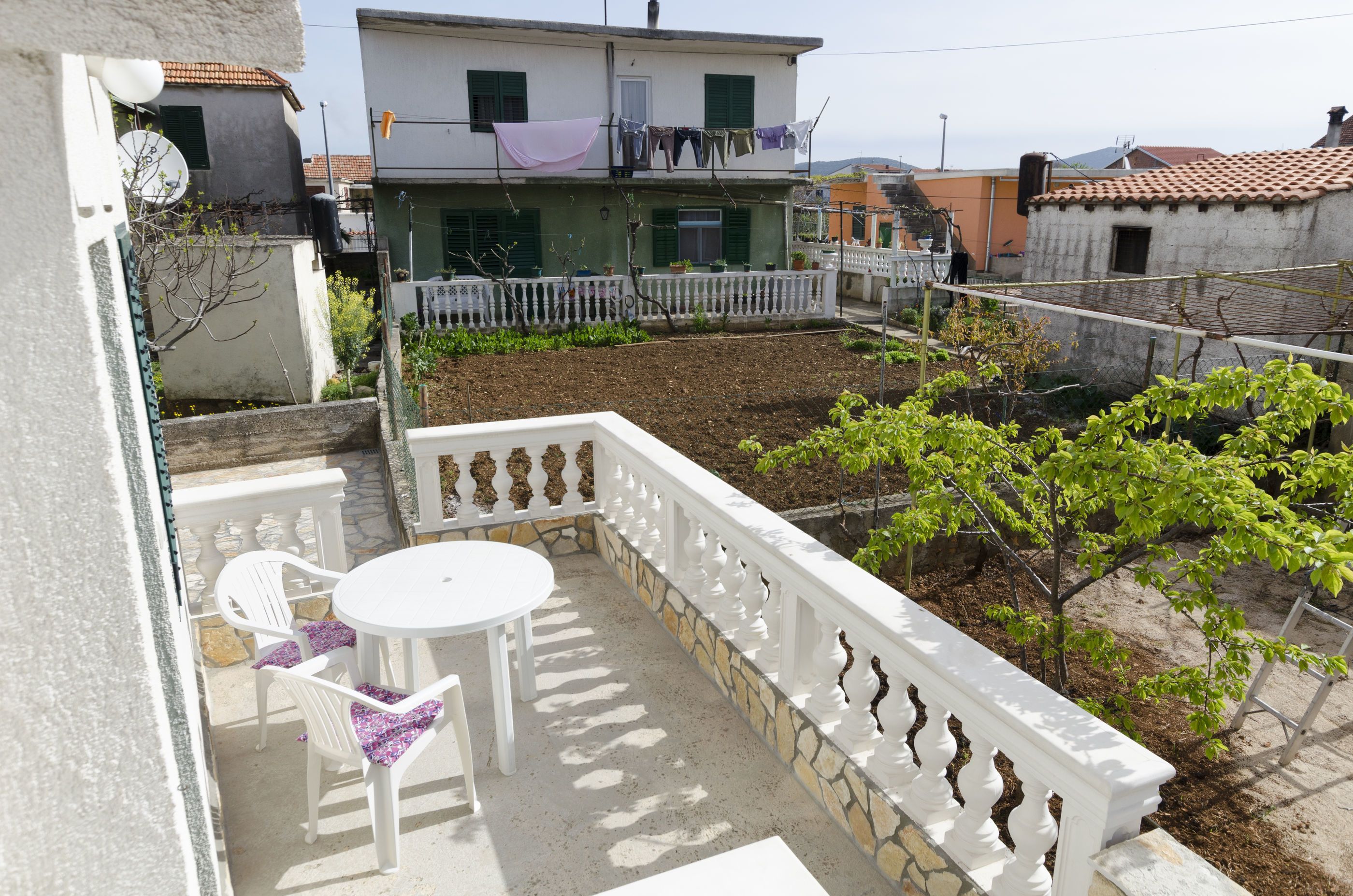 Un balcon avec une table et des chaises blanches, une balustrade blanche et une vue sur les immeubles voisins.