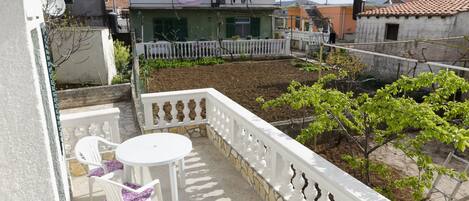 Un balcon avec une table et des chaises blanches, une balustrade blanche et une vue sur les immeubles voisins.