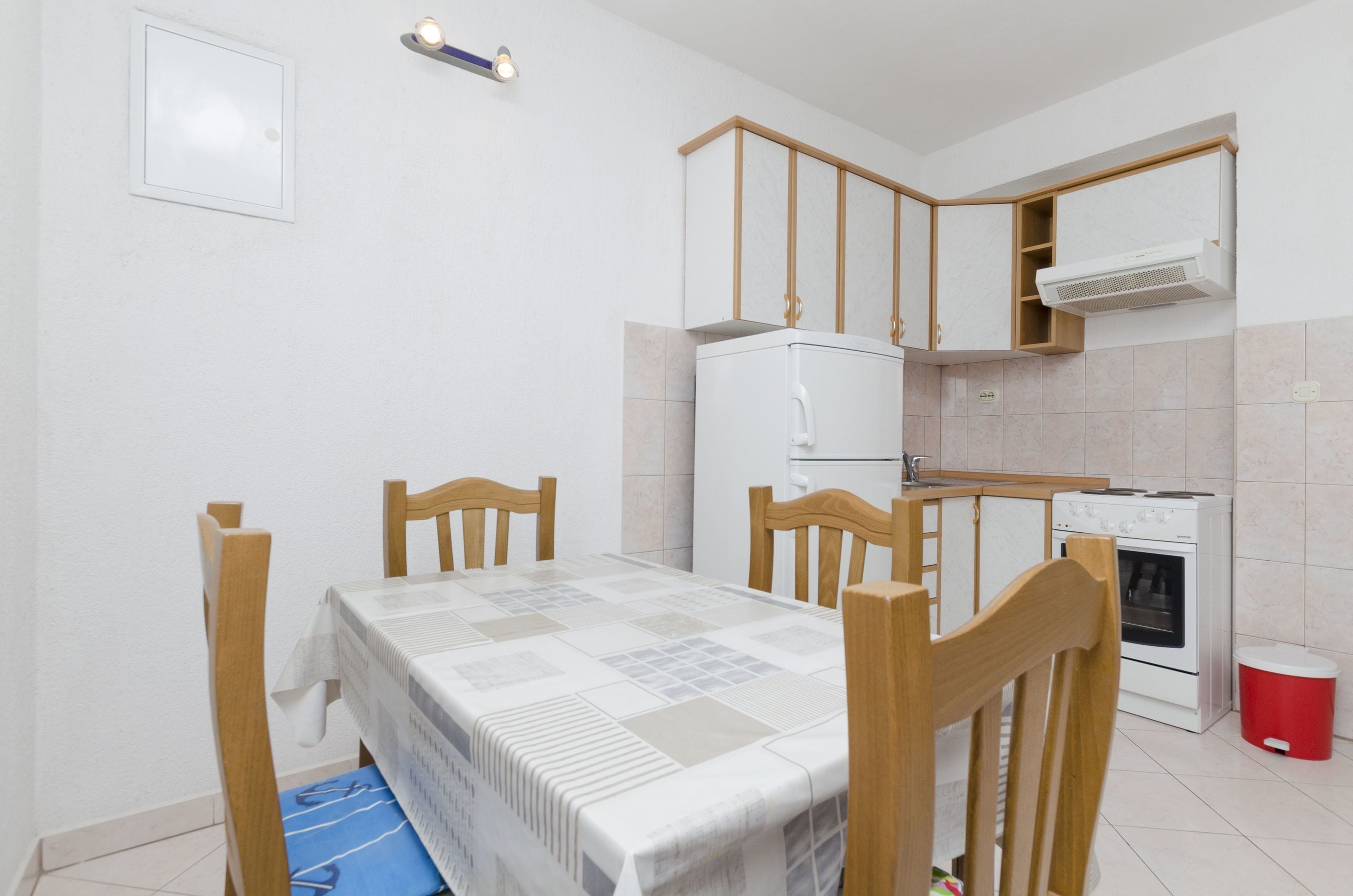 A compact kitchen with a dining table, chairs, a white refrigerator, a stove, and an air conditioning unit.