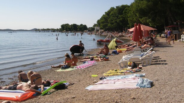 Ein Strand mit badenden Menschen, Liegestühlen und einem Boot auf dem Wasser.