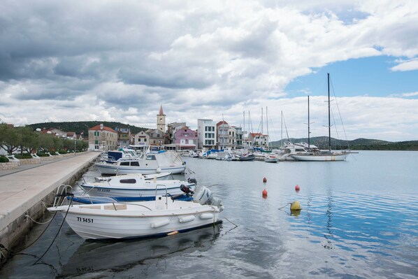 A marina with several boats docked, a church with a bell tower, and a hillside in the background. - Apartments Mime (Pirovac)