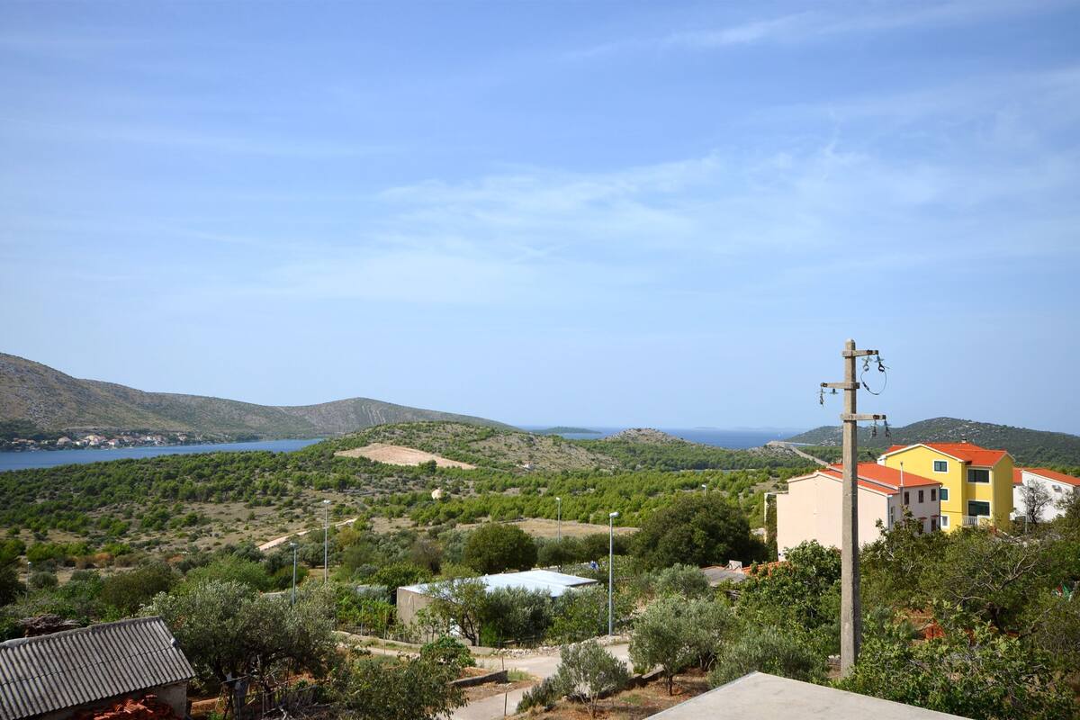 Un paysage côtier offrant une vue sur la mer, des collines et un bâtiment doté d’un toit rouge.