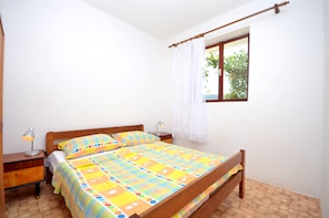 A bedroom with a wooden bed, a nightstand, a lamp, and a window with a curtain. - Apartments Kata (Sibenik)
