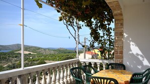 Ein Balkon mit Tisch und Stühlen, mit Blick auf eine schöne Landschaft mit Hügeln und einem Gewässer.