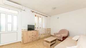 Ein Zimmer mit Holzboden, einem beigefarbenen Sofa, einem roten Sessel, einem Holzschrank und einem Fernseher.