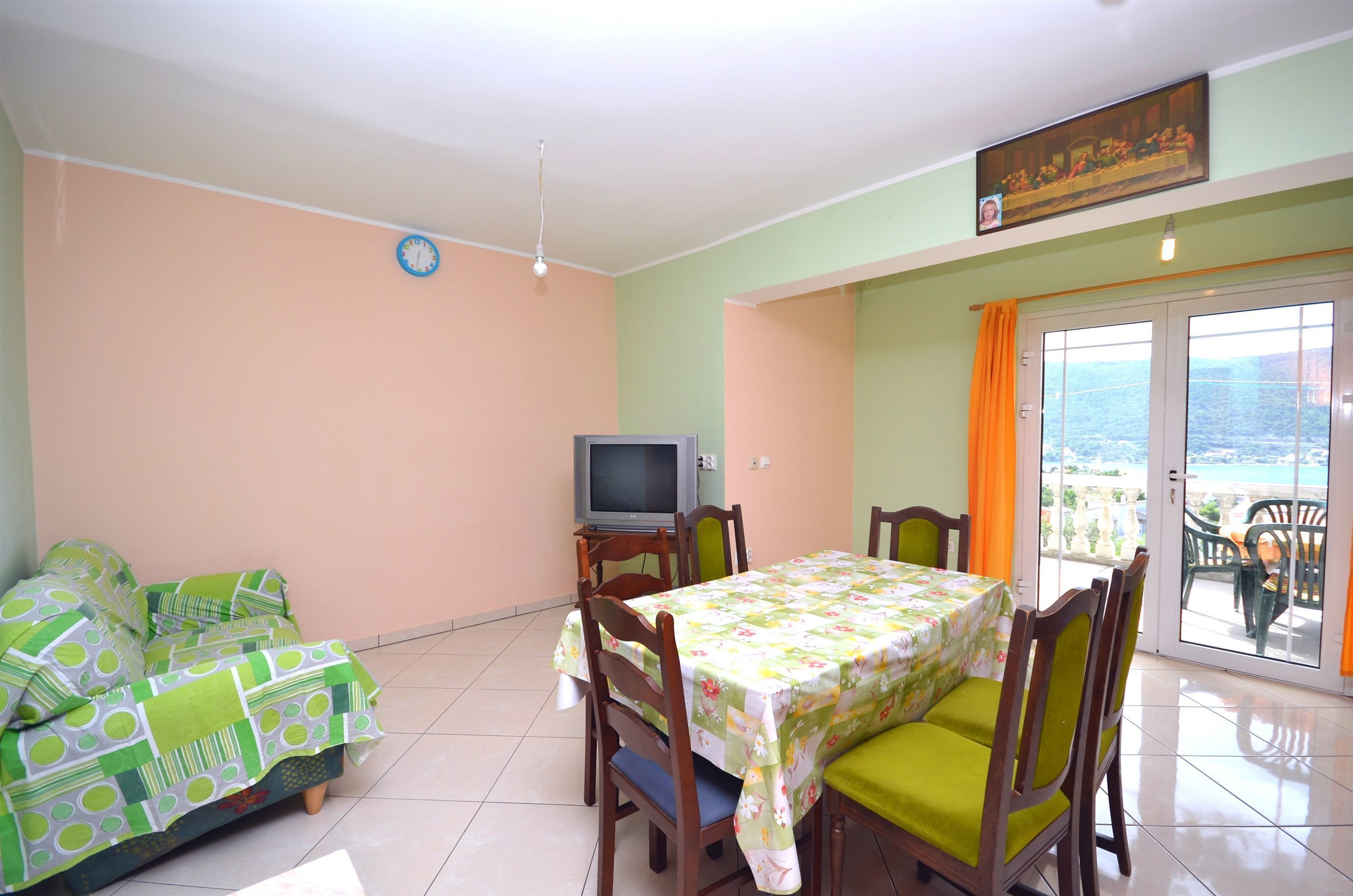A dining area with a table set for four, a sofa, a television, and a balcony with a view.
