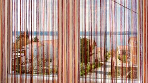 A view through a window with vertical blinds, featuring a coastal landscape with buildings and a clear sky. - Apartments Bregovec Maslenica (Maslenica)