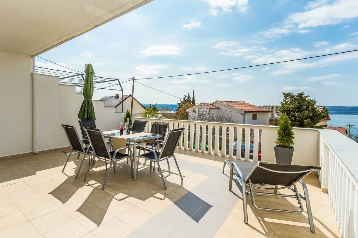 A balcony with a table and chairs, a potted plant, and a view of the sea.