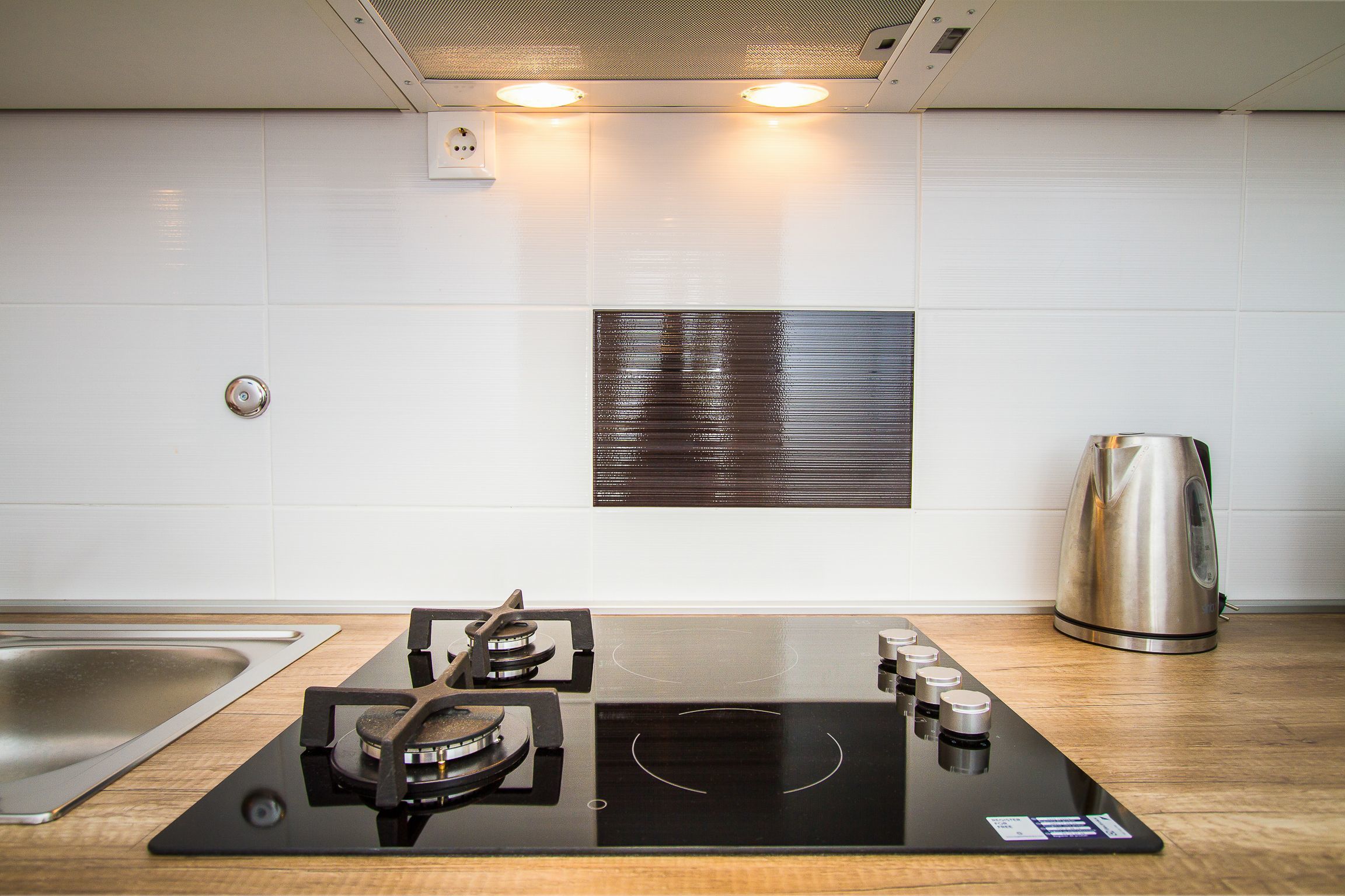 A modern kitchen with a built-in stove, a kettle, and a stainless steel sink.
