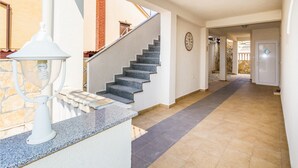 A hallway with a staircase leading to a second floor, a white wall clock, and a door with a diamond-shaped window. - Apartments Bregovec Maslenica (Maslenica)