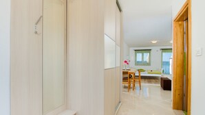 A hallway leading to a dining area with a table and chairs, a bench, and a window with green curtains. - Apartments Bregovec Maslenica (Maslenica)