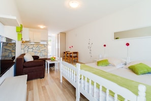 Una habitación moderna y bien iluminada con cama, sofá, mesa de comedor y zona de cocina.