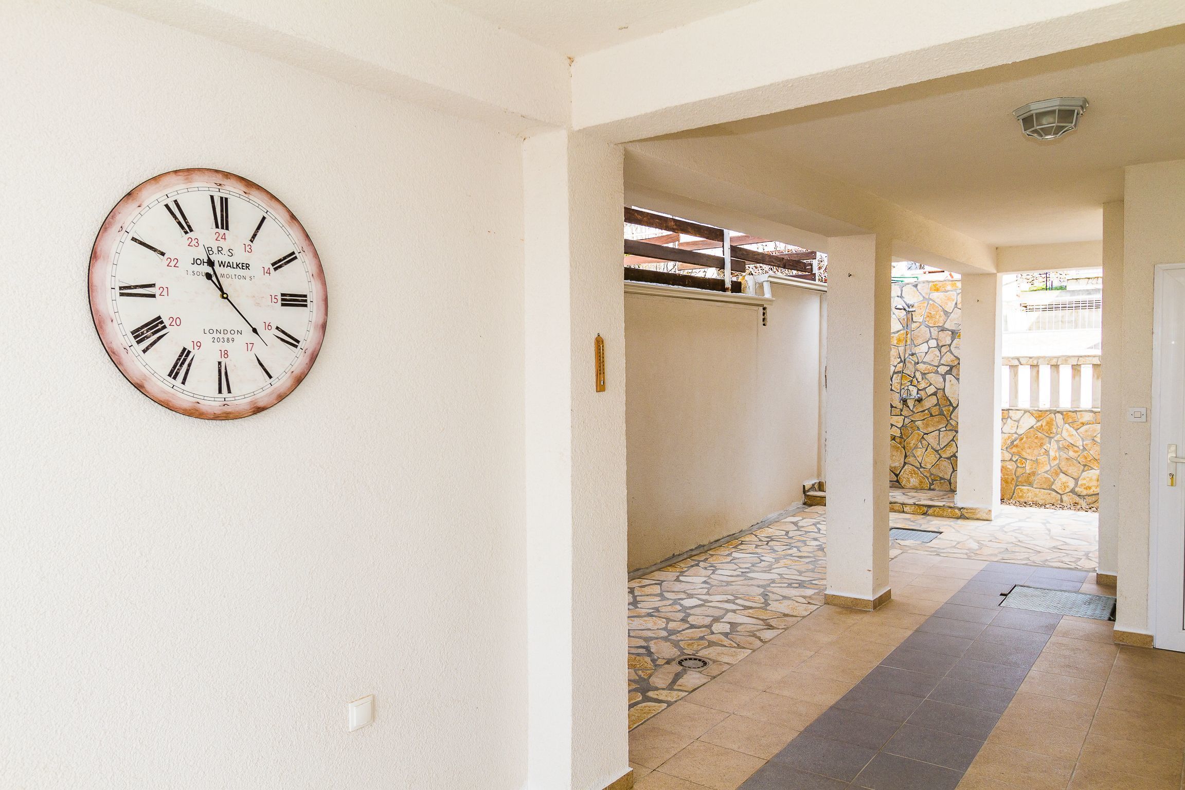 A hallway with a wall-mounted clock, a stone-tiled entrance, and a door leading to an outdoor area.