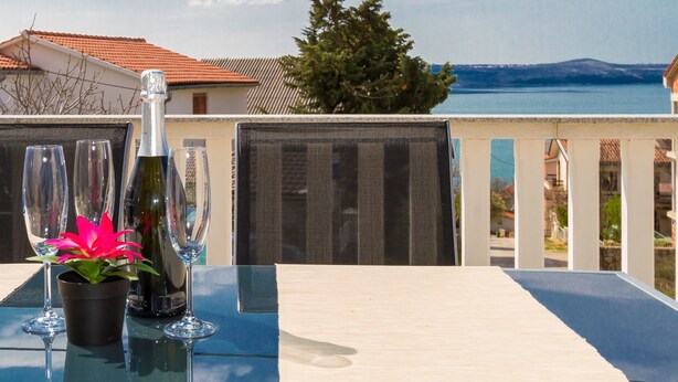 A balcony with a table set for a meal, overlooking a body of water and houses. - Apartments Bregovec Maslenica (Maslenica)